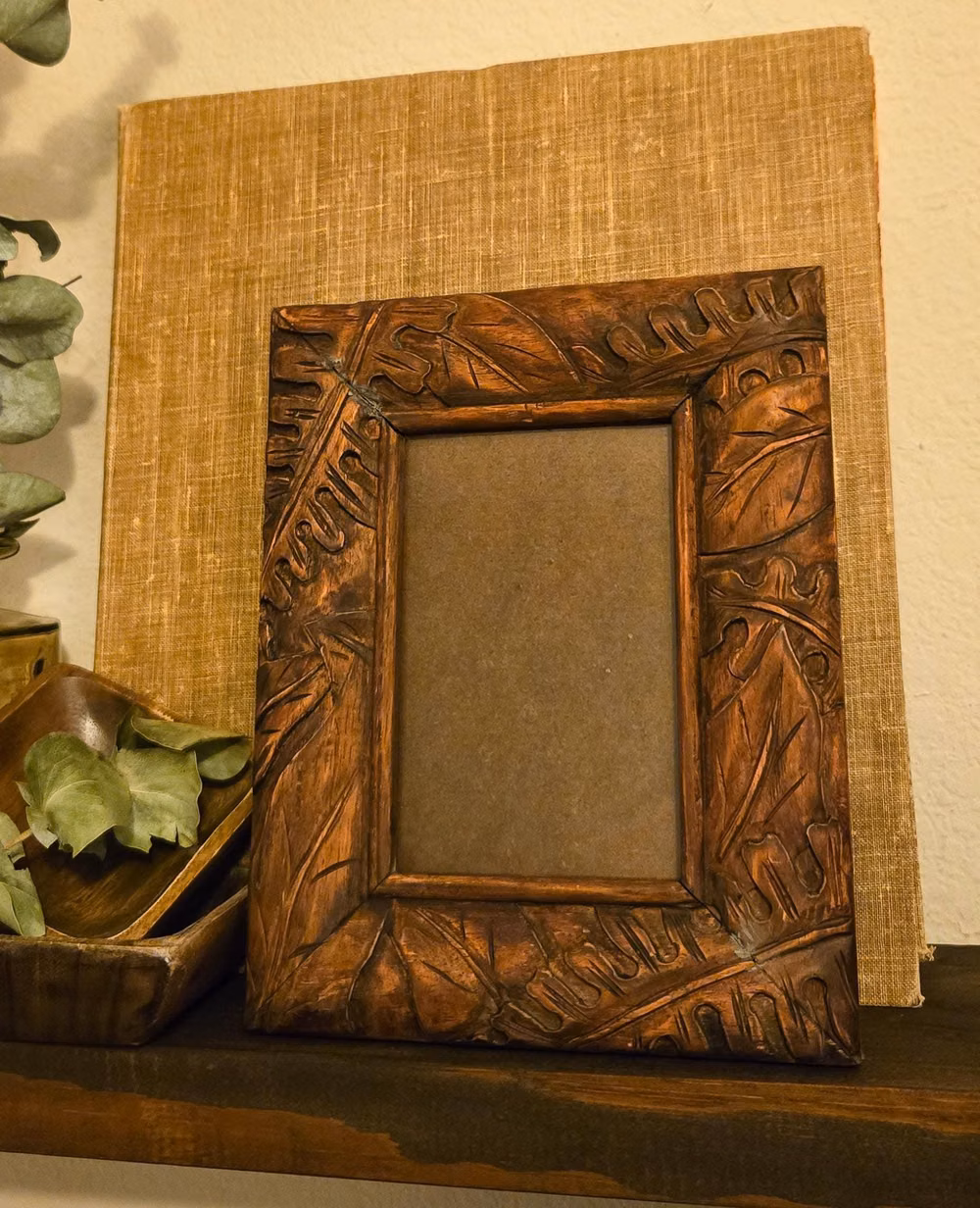 intricate hand carved wood leaf detail photograph - Some frames are the art. A vintage hand-carved wood picture frame -- deep relief tropical botanical carving covering every inch of the surface, large overlapping leaves, organic forms, and a warm dark copper-brown finish that deepens into shadow at every carved edge. Glass and easel back both included and intact. Holds a 4×6 photo. 🌿🖤 Stand it on a bookshelf, a nightstand, a writing desk, or a mantle. The kind of frame where whatever you put inside almost becomes secondary -- the frame itself commands the room. Empty it looks sculptural. Filled it looks intentional. ♥︎ Details Era: 1980s-1990s Style: Dark Botanical / Global Folk Art / Boho Maximalist Material: Solid hand-carved wood, glass Dimensions: 9.5"H × 7.5"W | Fits 4×6 photo Weight: Approx. 0.8 lbs Condition: Good vintage conditio