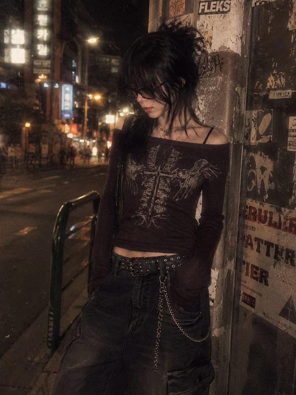 Grunge aesthetic - Moody cyber grunge outfit inspired by underground Korean street fashion and dark Y2K aesthetics. The look features an off-shoulder gothic graphic top with cross artwork, oversized black cargo pants, layered chain accessories, studded belt details, and messy alternative styling for a rebellious late-night streetwear vibe. The dim city lighting, blurry neon background, and distressed urban textures create a cinematic indie sleaze atmosphere perfect for Pinterest fashion inspiration boards. This outfit blends dark feminine energy with punk-inspired streetwear, alternative fashion, and modern Seoul nightlife aesthetics. Ideal for fans of grunge outfits, goth street style, underground fashion photography, and edgy monochrome styling with silver accessories and relaxed silhouettes. Perfect inspi
